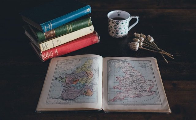 An open atlas with other books and a cup of tea. Expats and immigrants.