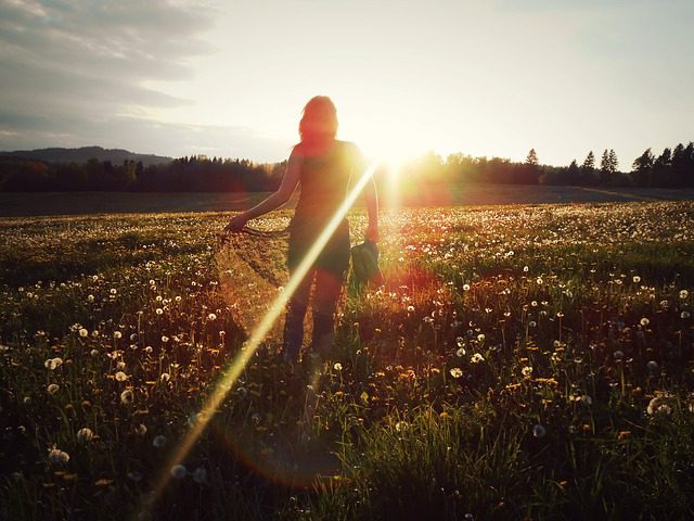 Young woman in a field facing the sun as it sets.