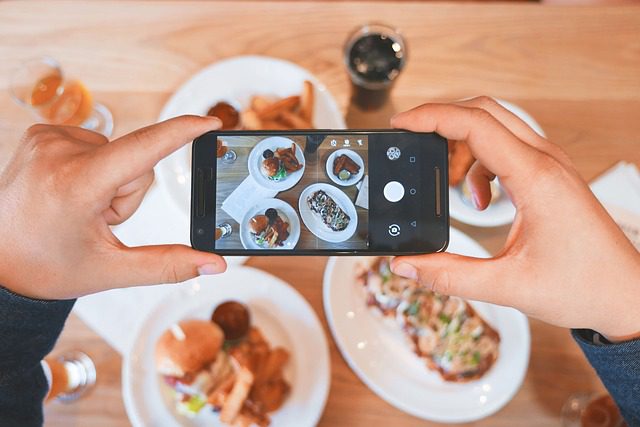 Two hands holding a smartphone photographing their food.