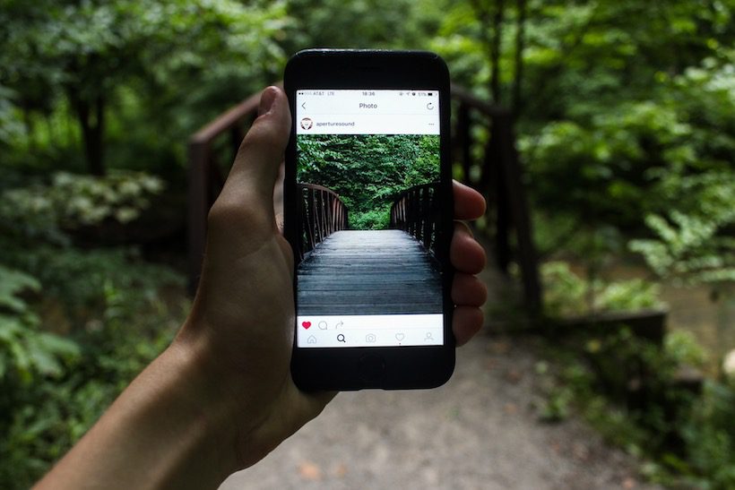 Hand holding a smartphone taking a picture of a bridge for social media.