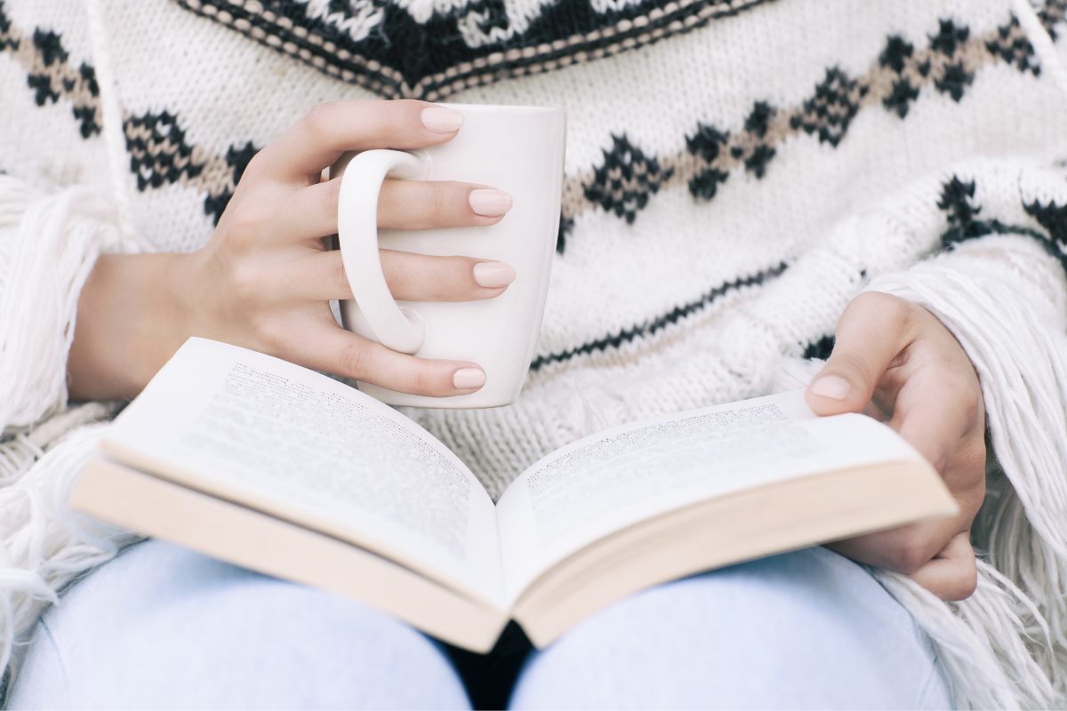 Female hands holding a book and a cup of coffee