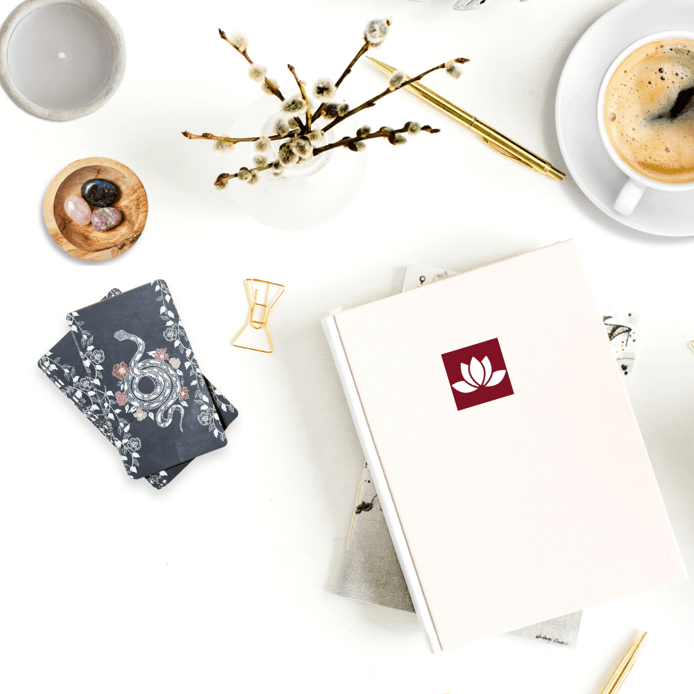 A journal and other stationery, cup of coffee, tarot cards, candle, and a bowl with crystals.
