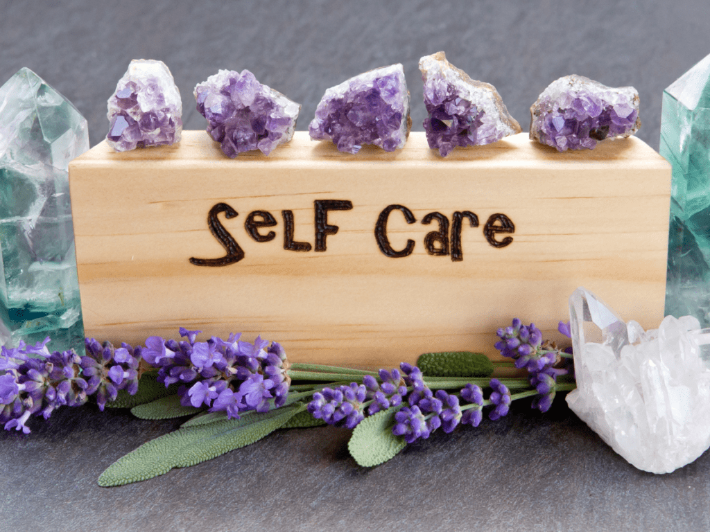 Self-care - word burnt in wood with purple lavender flowers, amethyst, fluorite and quartz crystals on a slate background.