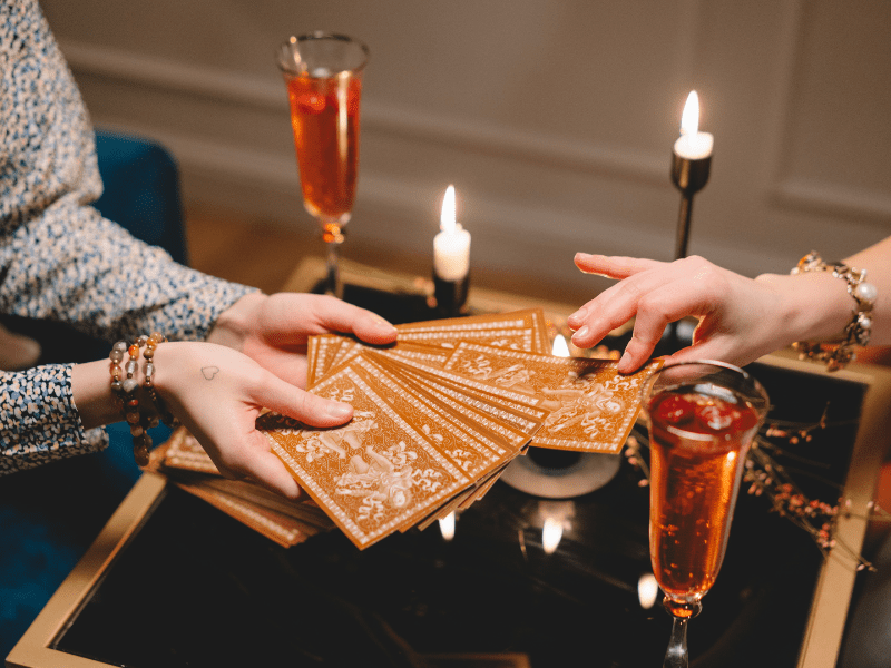 Two women sitting across from each other touching tarot cards.