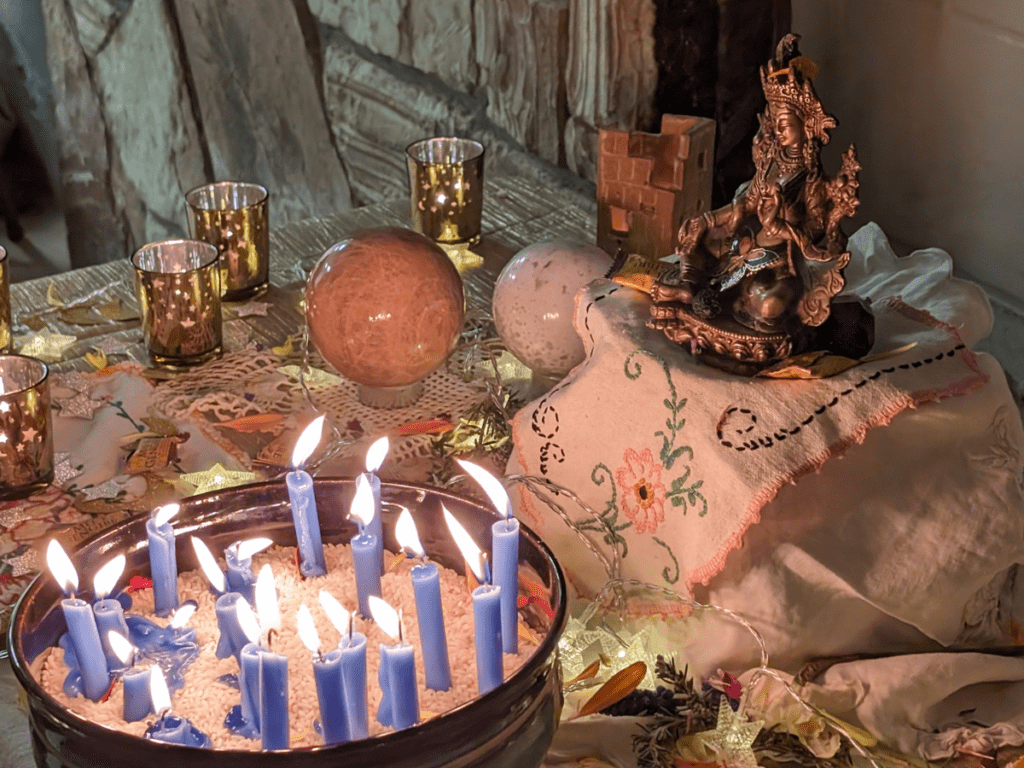 An altar with a statue of Tara, a bowl filled with lit candles, and other items.