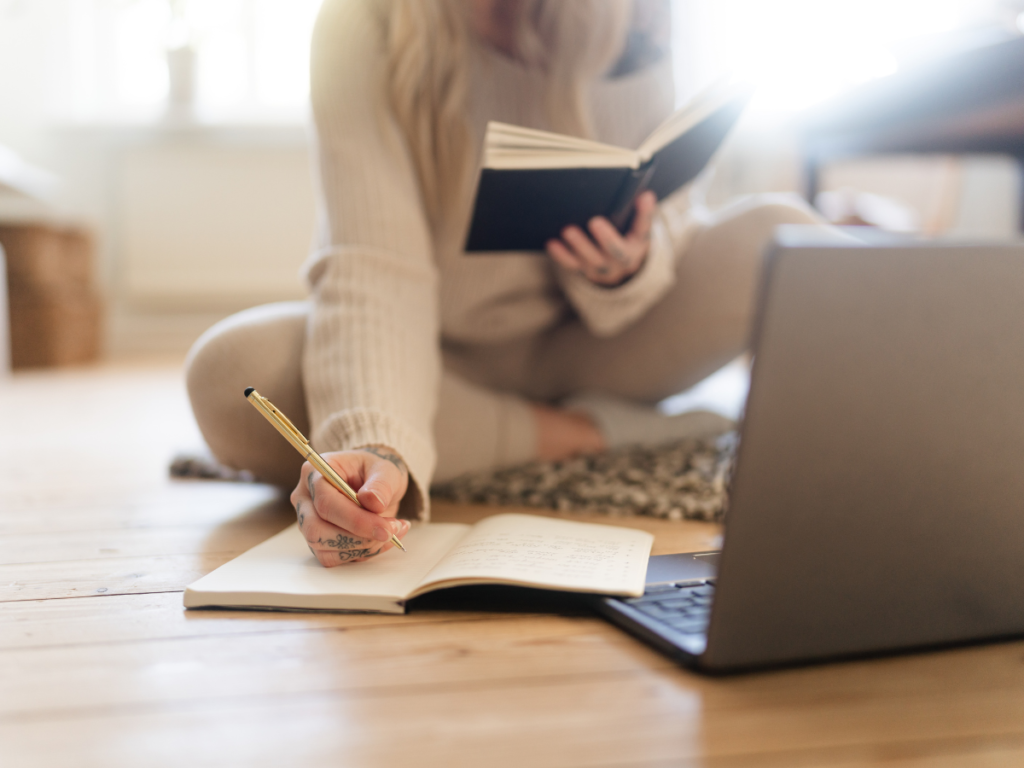 A woman with a book, laptop, and notebook doing research on decolonising Pagan practice.