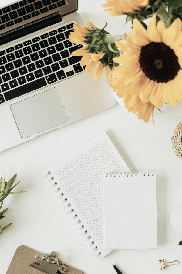 A laptop, notebooks, and sunflowers.