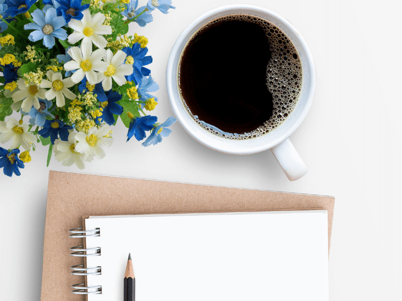Flowers, a cup of coffee, and journals with a pencil.