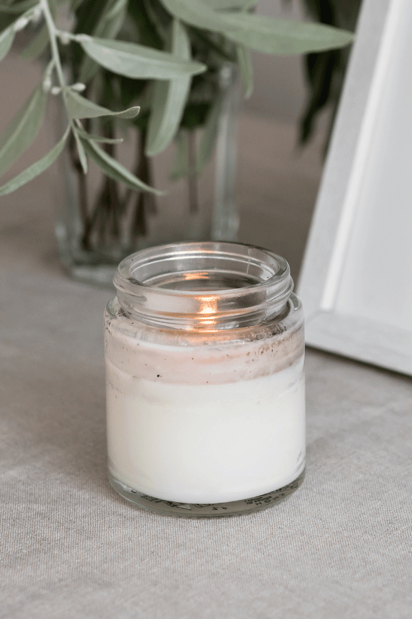A lit jar candle and greenery.