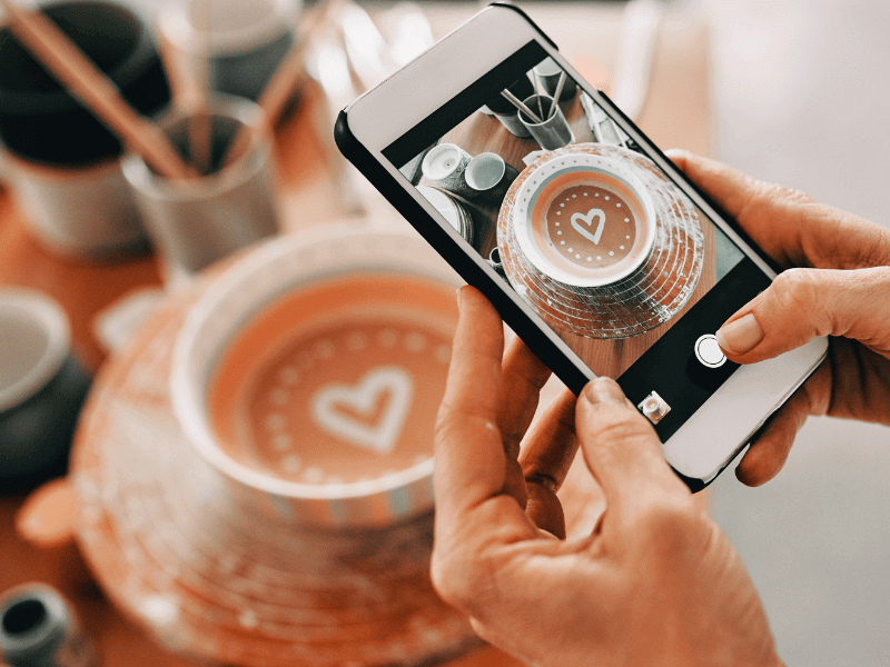 Hands holding a smartphone taking a photo of pottery for social media.