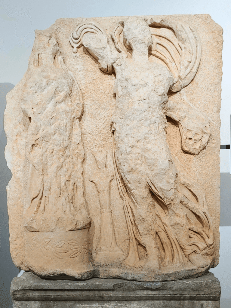 A broken and desecrated cult statue of the local Aphrodite of Aphrodisias being crowned by the draped figure of Greek Aphrodite.