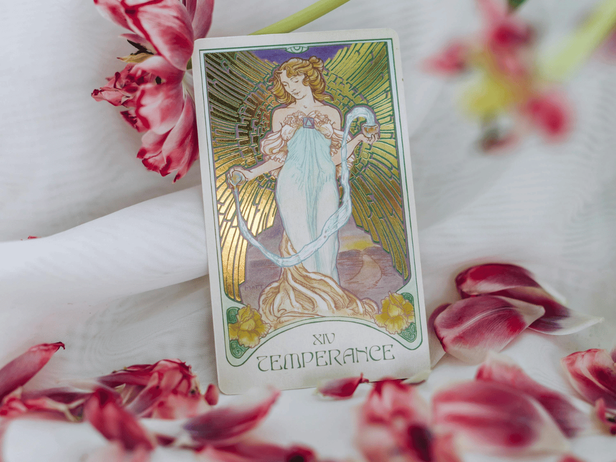 The Temperance tarot card against pink flowers.