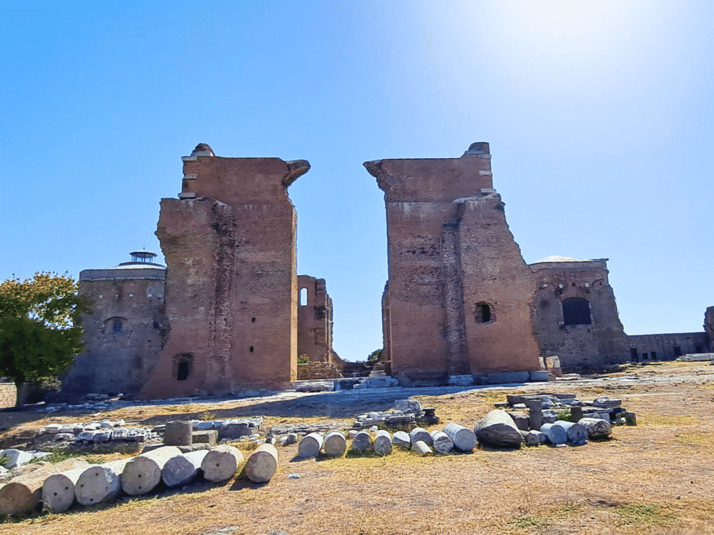 Wide view across the Red Hall ruins, with two massive brick wall sections, rotundas and rows of stone architectural fragments.