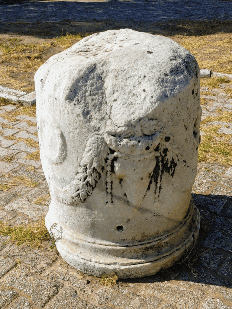 Weathered cylindrical marble fragment carved with a hanging garland and other decorative motifs.