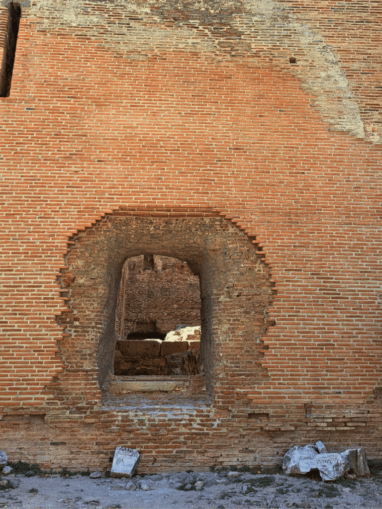 Small arched opening through a red-brick wall at the Red Hall, with carved stone fragments lying below.