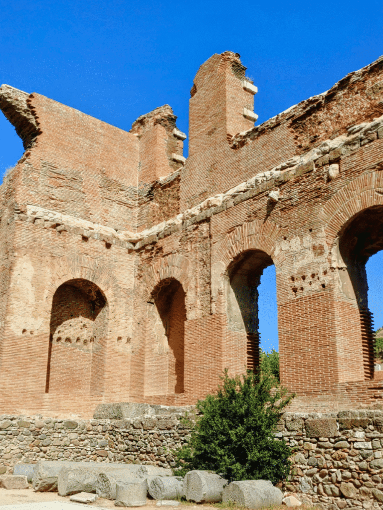 Tall red-brick walls with multiple arched niches and openings rising against a blue sky.