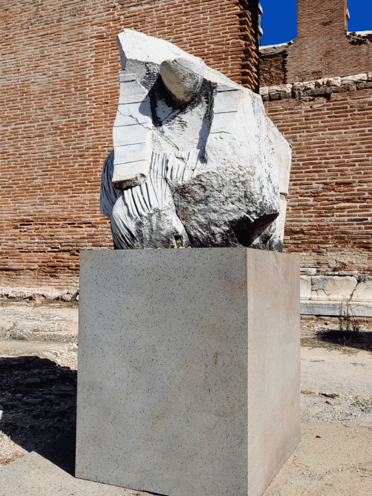 Fragment of a large Egyptianising stone figure wearing a striped nemes headcloth, displayed against a red-brick wall.