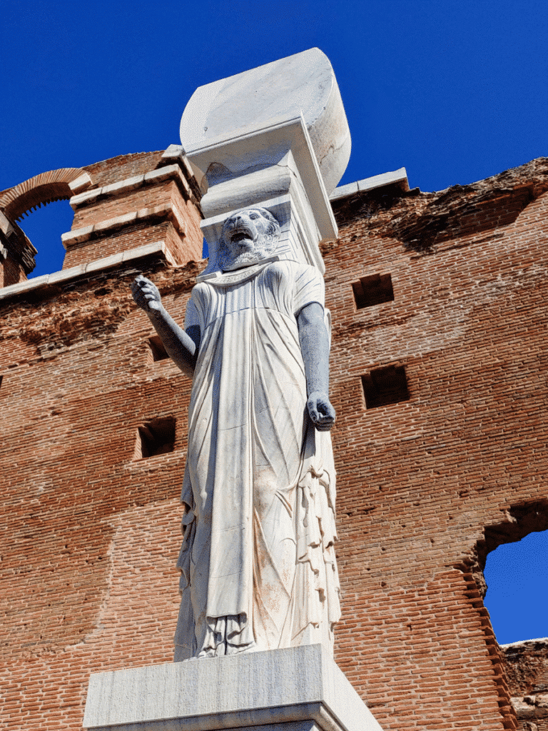 Reconstructed lion-headed figure wearing a nemes headcloth and long draped garment, supporting an architectural element above its head.
