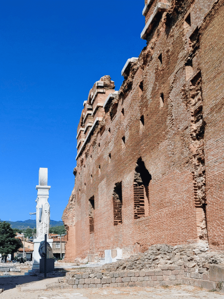 Long red-brick wall of the Red Hall rising against a blue sky, with a reconstructed Egyptianising figure visible at one end.