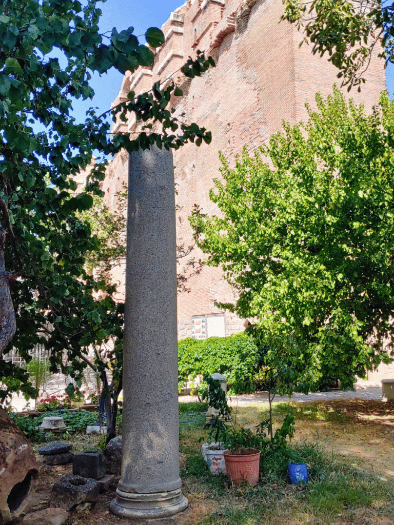 Tall grey stone column standing among trees beside the brick walls of the Red Hall.