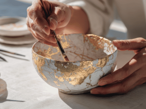 Ceramic artist applying golden leaf details with a fine paintbrush onto a bowl.